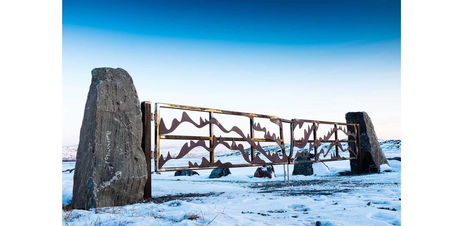 Upstanding stone pillars and a weathering steel gate mark the cemetery entrance…