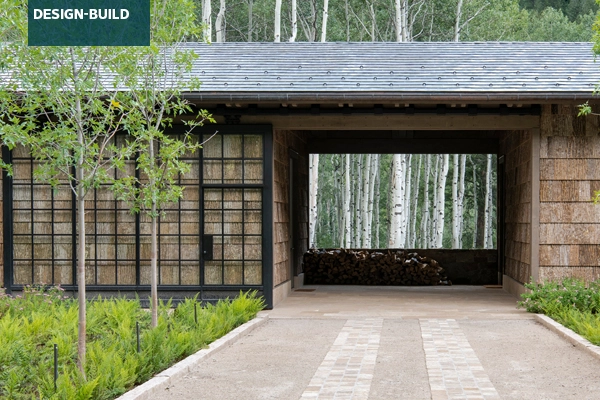 A breezeway with a rolling door links the home and garage, framing a painterly vignette of columnar aspen trees. A grid of trees line the courtyard, softened by a dense planting of ferns and native shrubs.